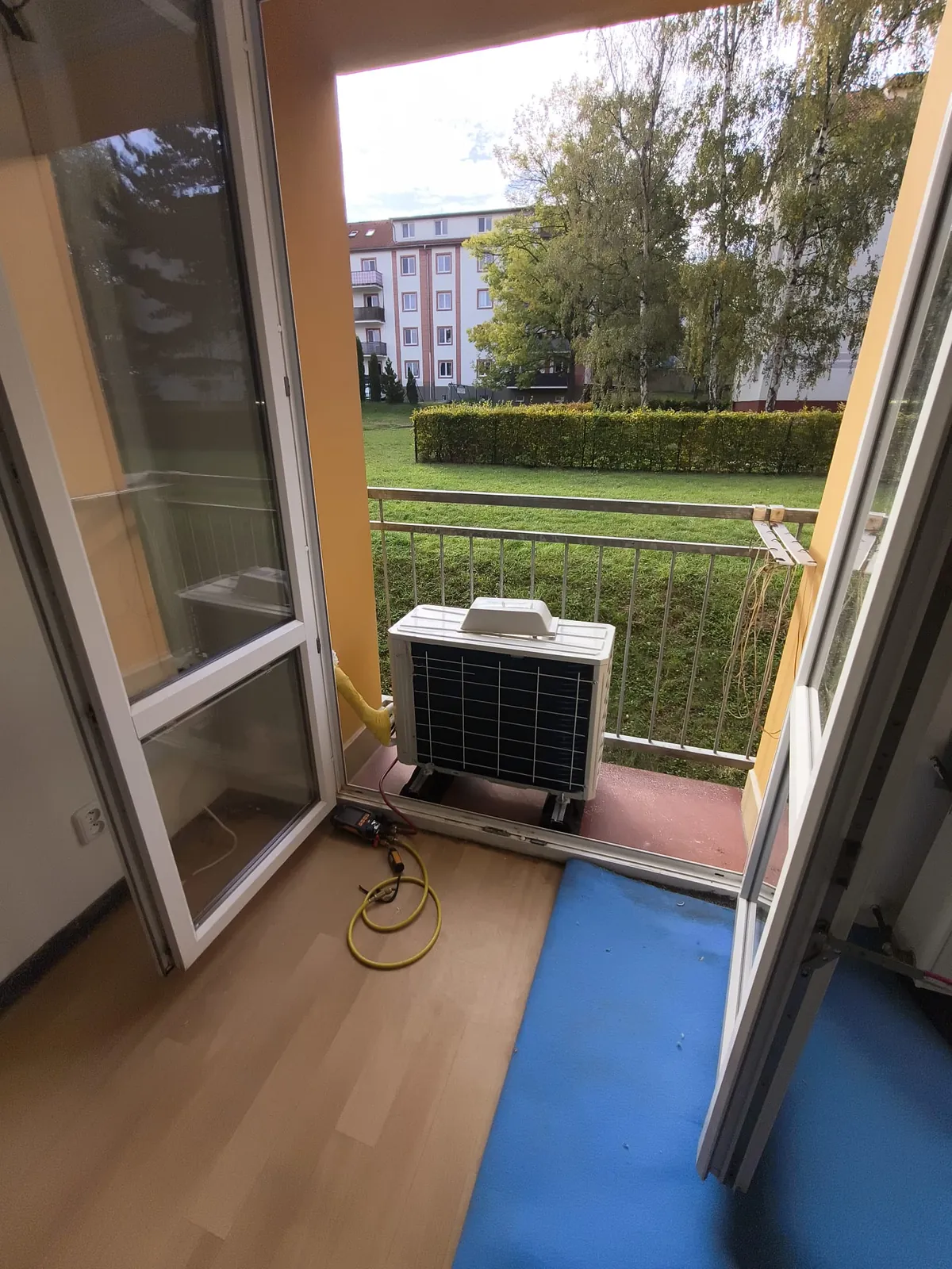 Venkovní jednotka na balkonu a měřicí souprava se žlutými hadicemi na podlaze
